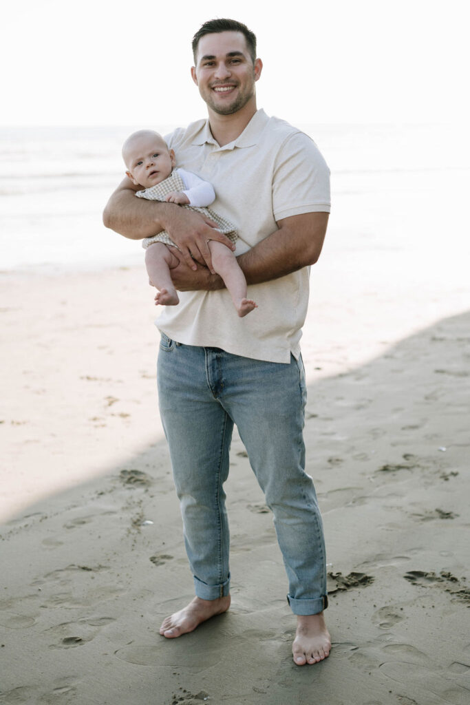 dad holding his newborn during their beach family photoshoot